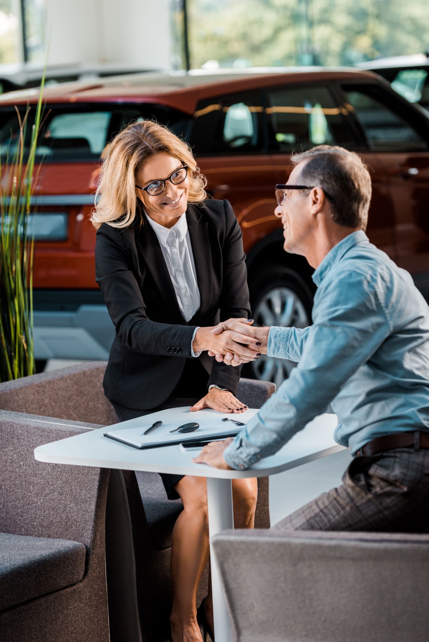 adult customer and female car dealer shaking hands in showroom