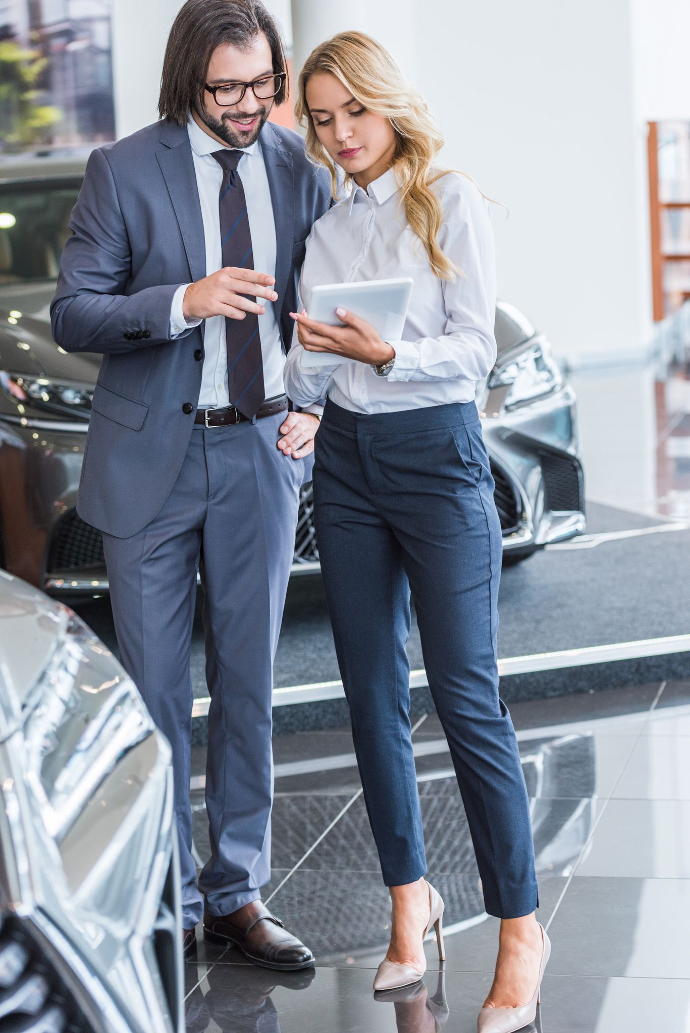 female auto salon seller with tablet helping businessman to choose car at dealership salon