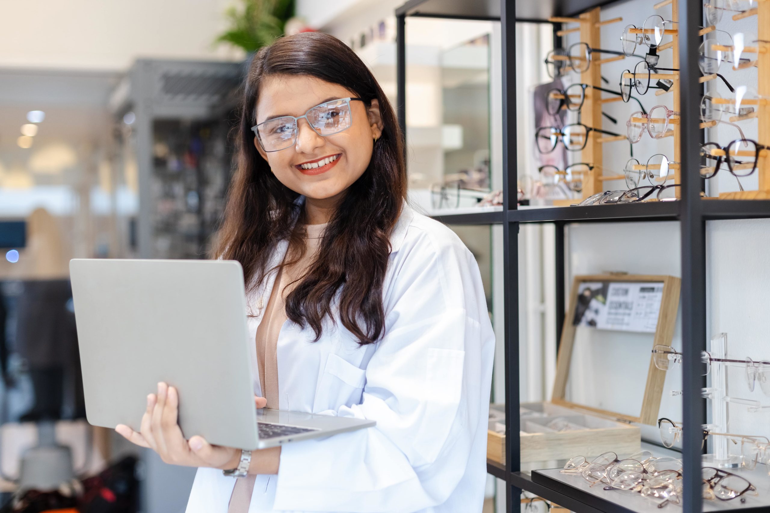 a woman holding a laptop in front of a display of glasses