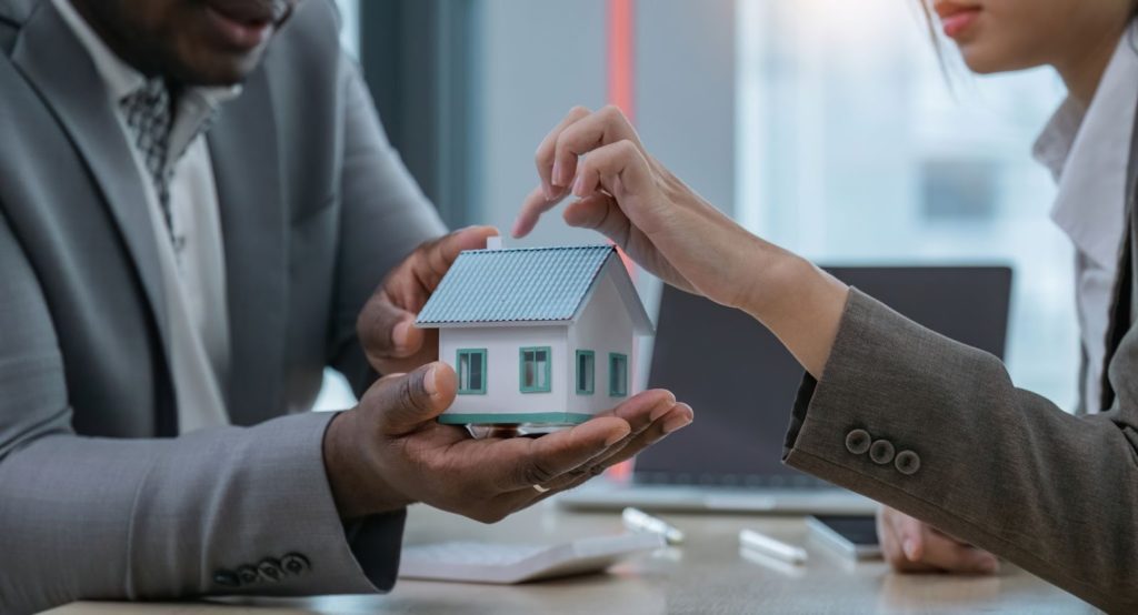 A man and woman holding a house model, symbolizing home ownership and partnership.