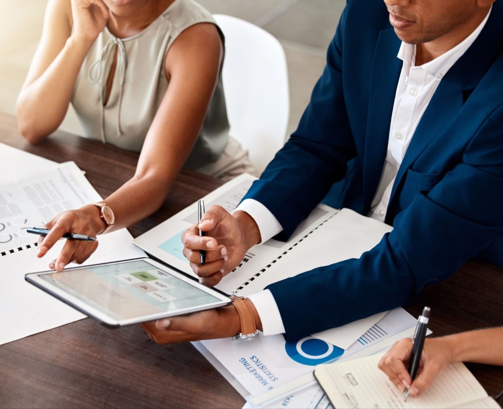 a man and woman sitting at a table using a tablet talking marketing