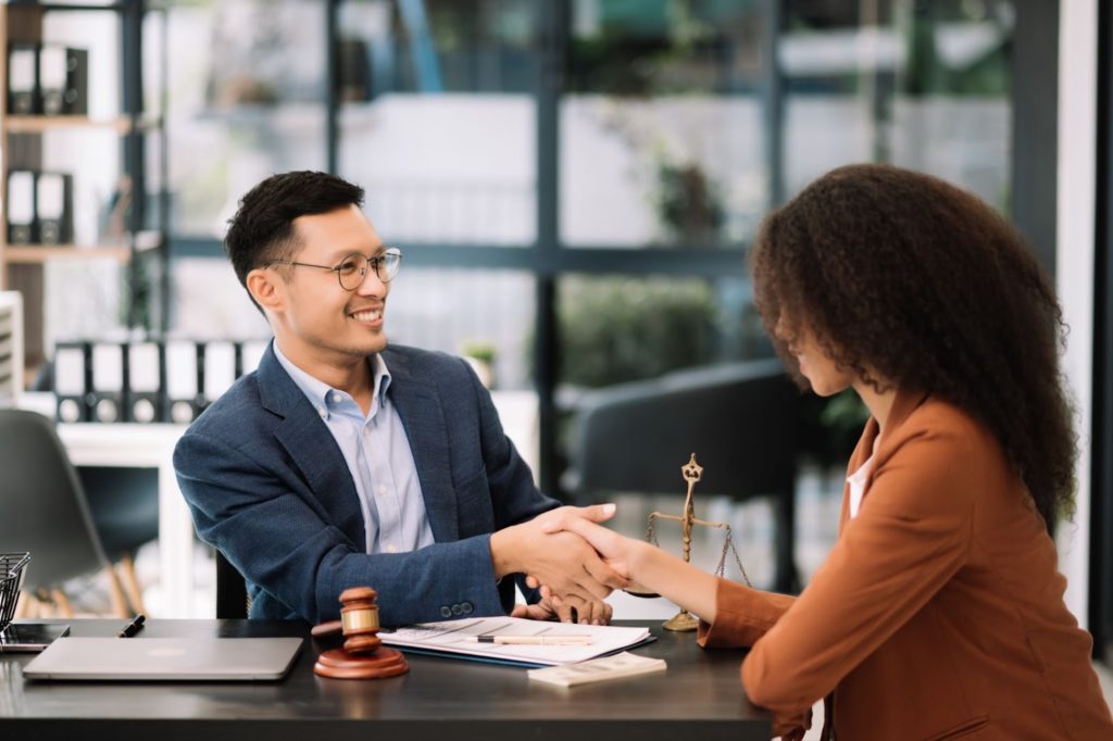 A man and woman shaking hands at a desk in a law firm office.