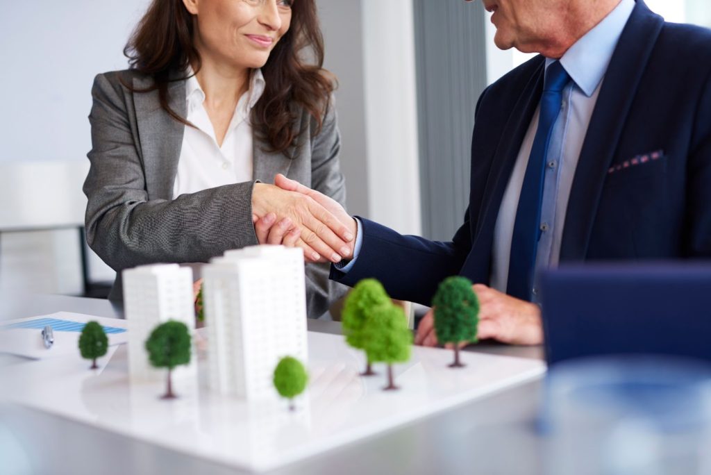 Two business professionals shaking hands over a table with a model of a house, symbolizing a successful real estate transaction.