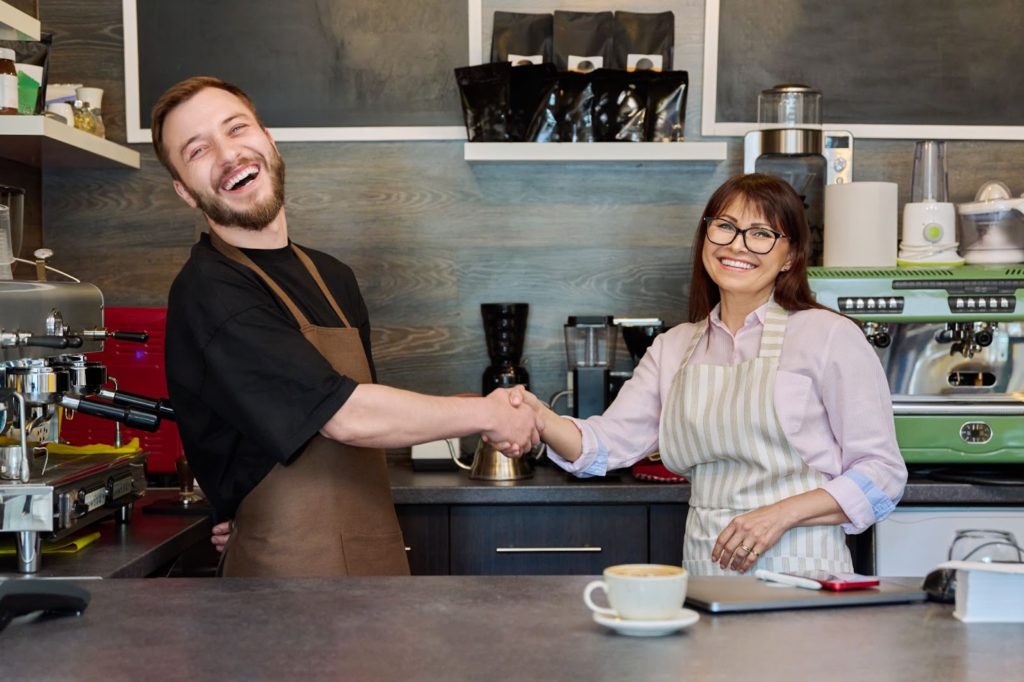 A man and woman shaking hands in a coffee shop, symbolizing a professional agreement or friendly interaction.