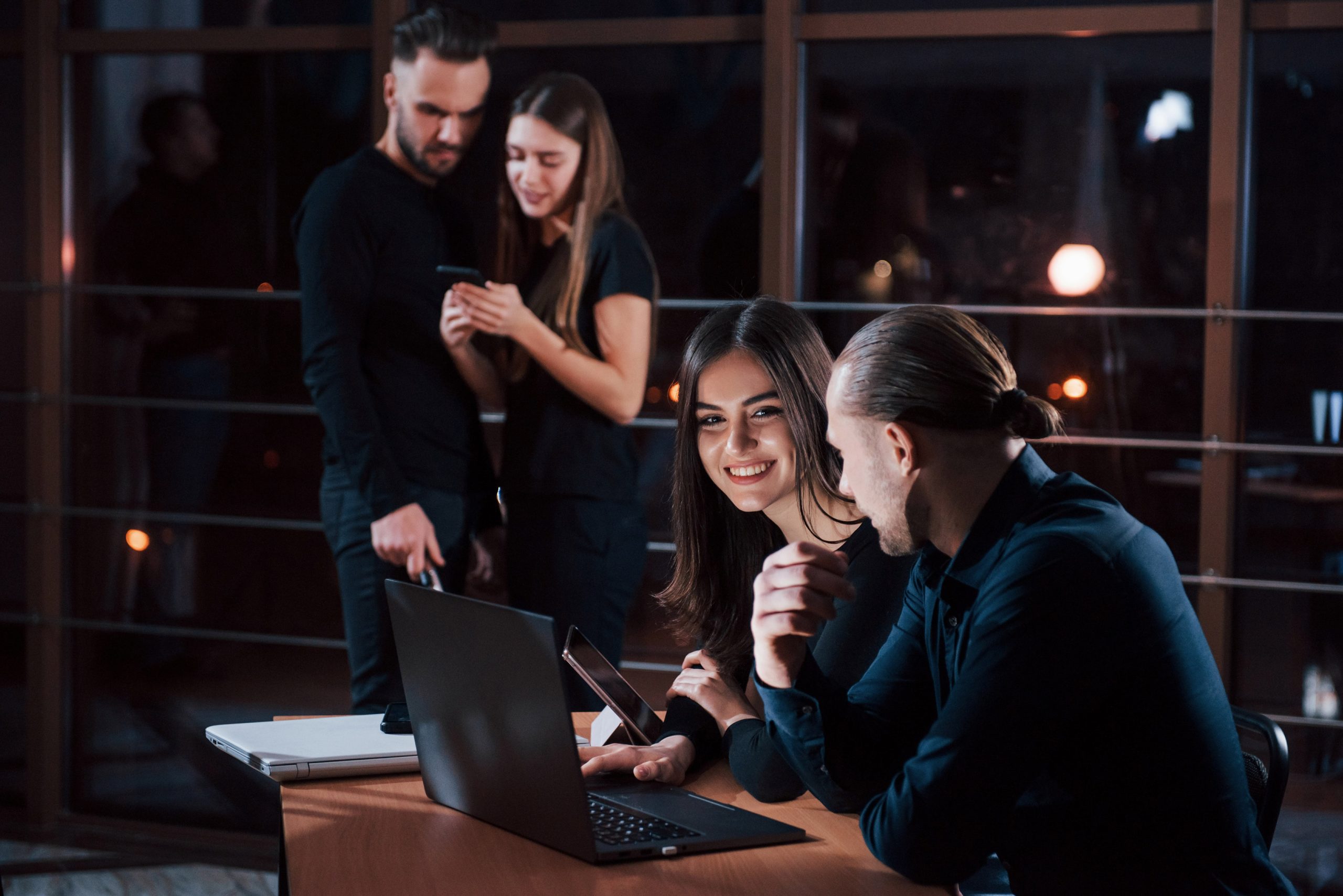 a group of people sitting at a table with laptops and a woman looking at a laptop