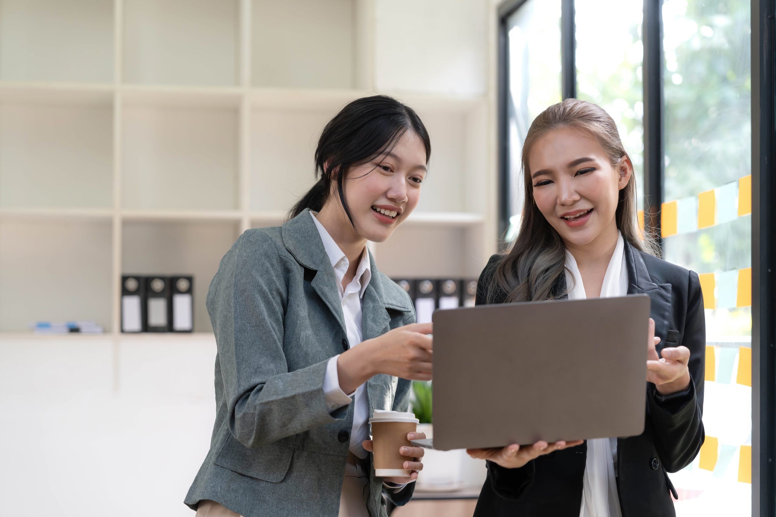 two women holding a laptop and a cup of coffee