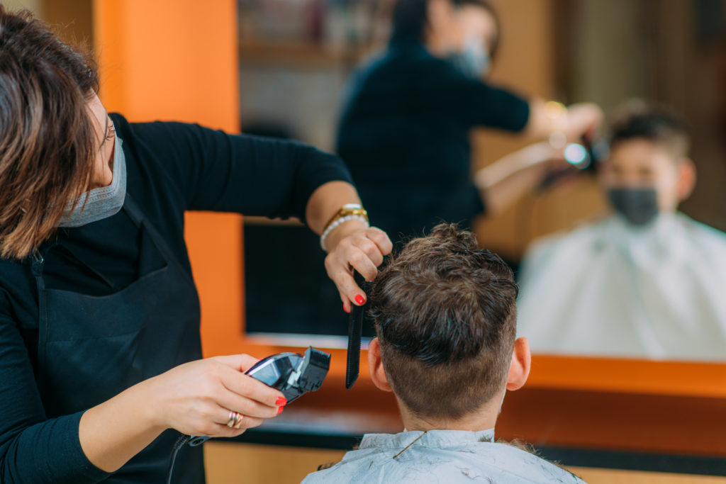 Boy having his hair cut in hairdresser's salon, wearing a protective mask