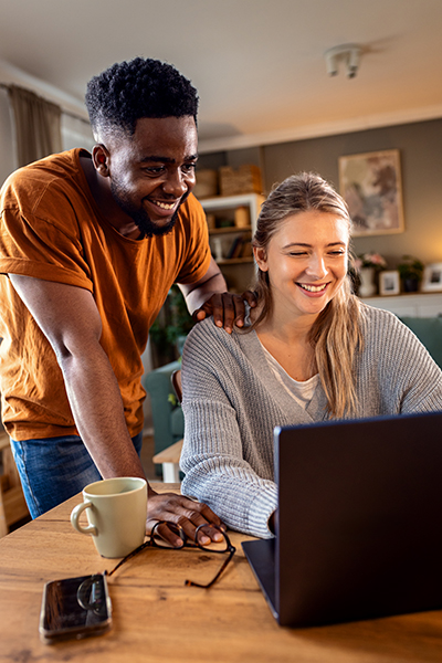 Smiling young mixed couple using a laptop while working on their home finances.