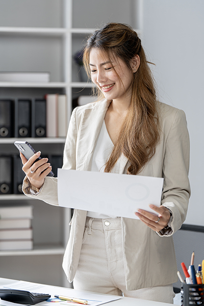 Small business entrepreneur looking at her mobile phone and smiling while communicating with her office colleagues