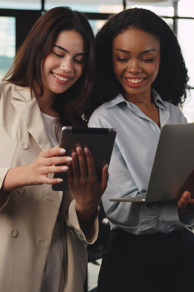 a couple of women looking at a tablet and a laptop