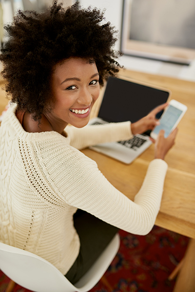 Portrait of an attractive young using her cellphone and laptop at home.