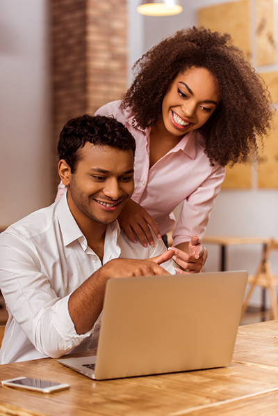 Young attractive Afro-American business couple using laptop, talking and smiling while working in cafe