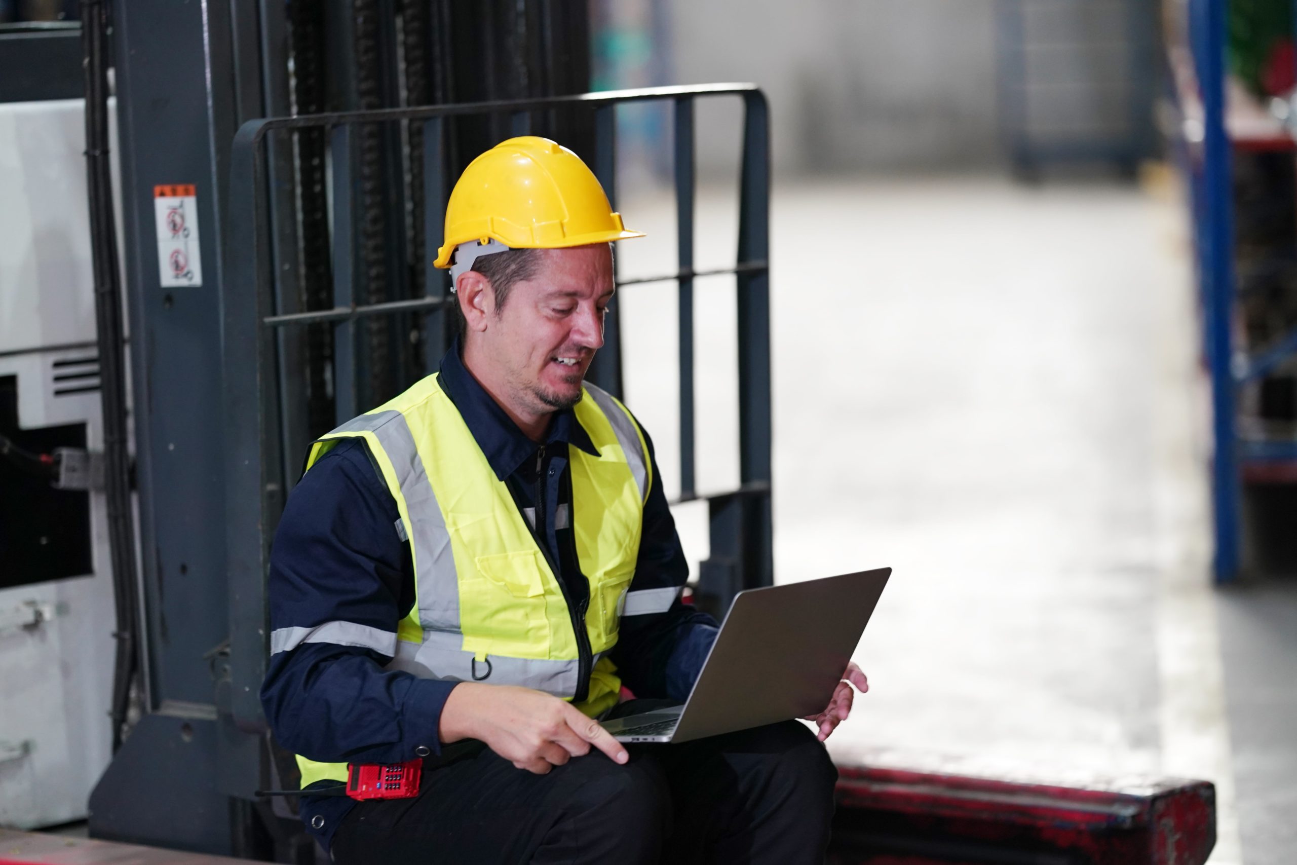 a man wearing a yellow hard hat and reflective vest sitting on a forklift