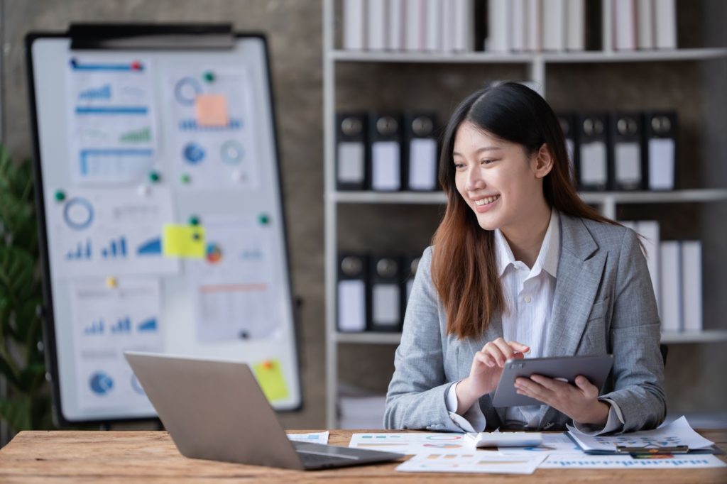 Business woman multitasking on laptop and tablet in an office setting.