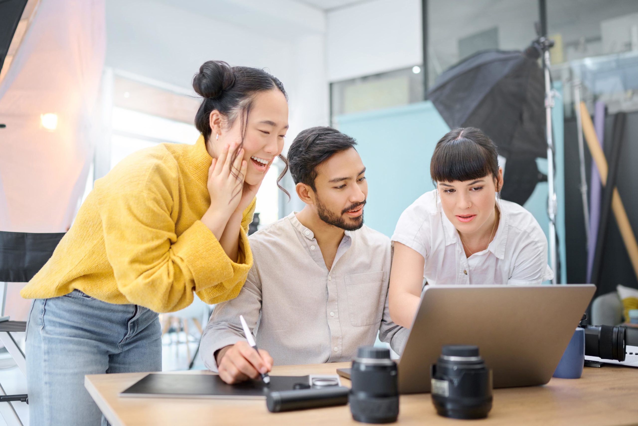 Office scene with three people working together on a laptop.