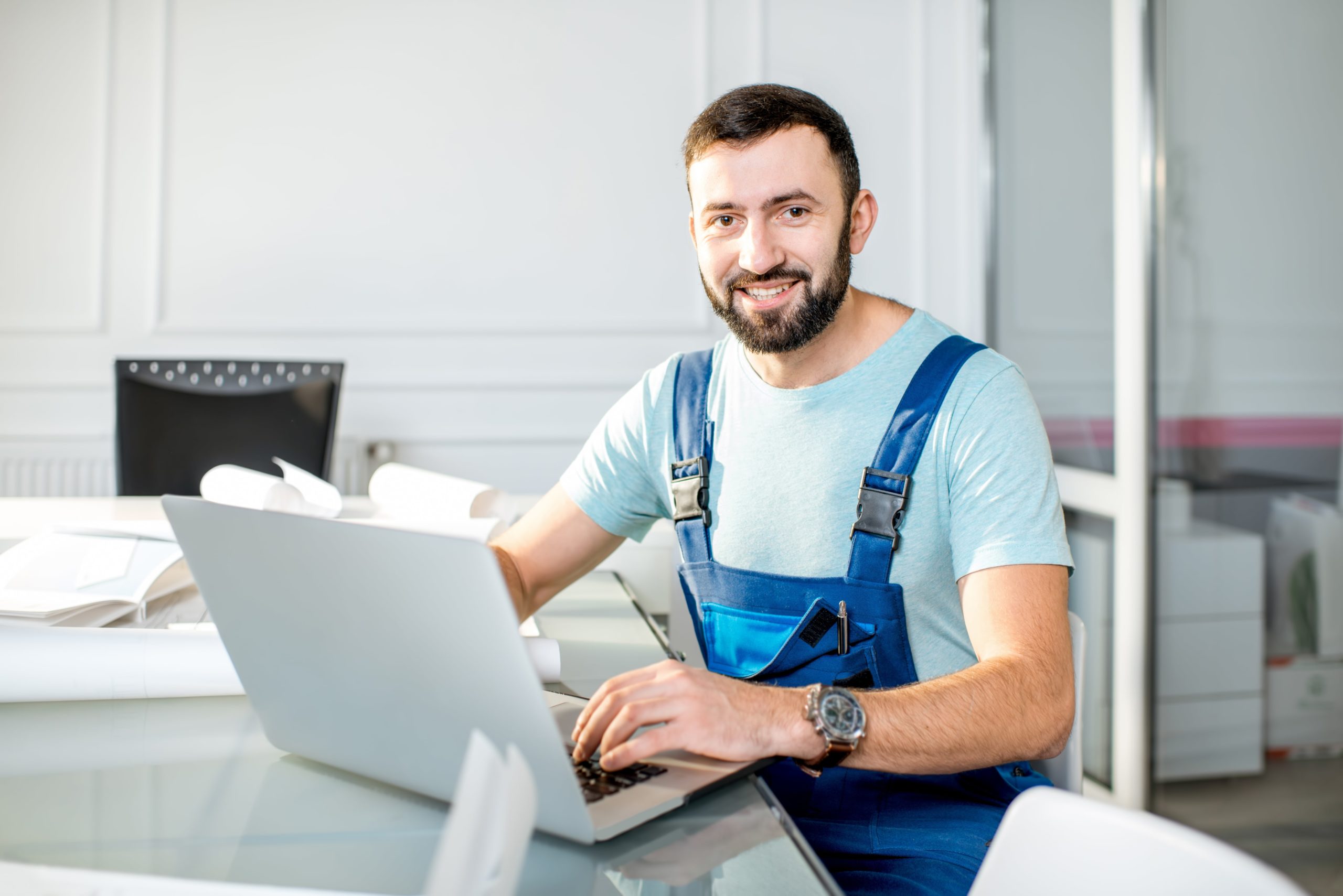 a man in overalls sitting at a desk using a laptop