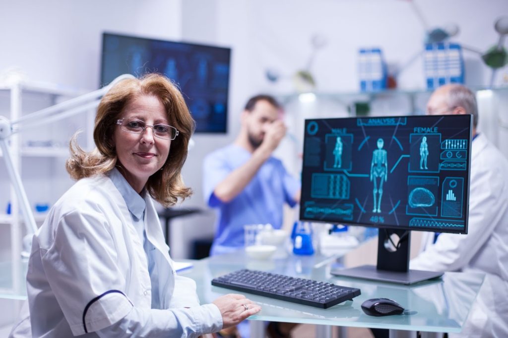 A female scientist in a lab coat is seated at a computer, conducting research and analyzing data.