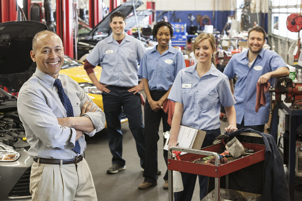 Portrait of smiling auto repair shop team with Pacific Islander owner