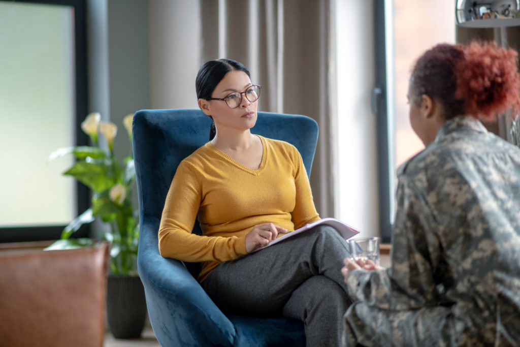 Asian psychoanalyst. Asian dark-haired psychoanalyst listening to woman wearing military uniform