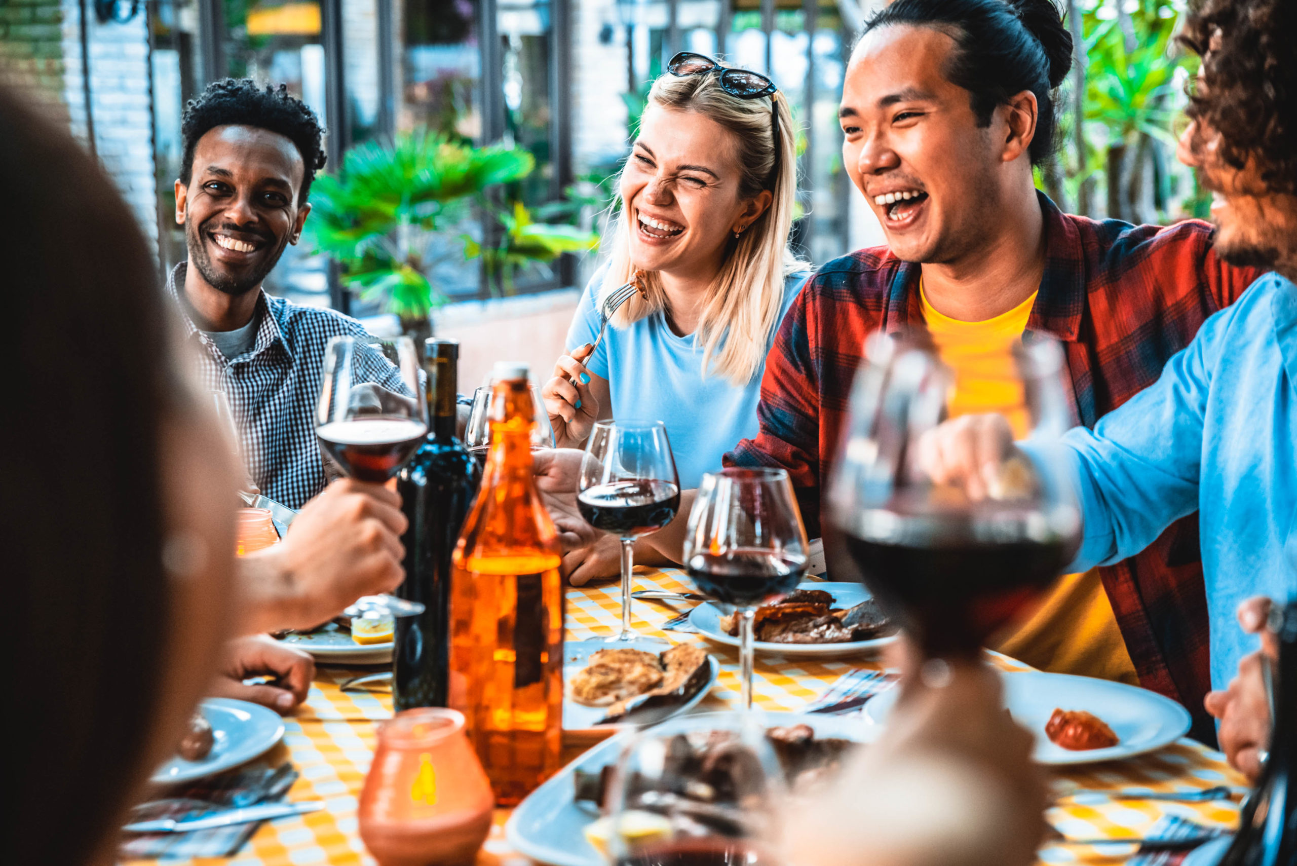 A diverse group of friends laughing and eating together at a dinner table, sharing a meal and enjoying each other's company.