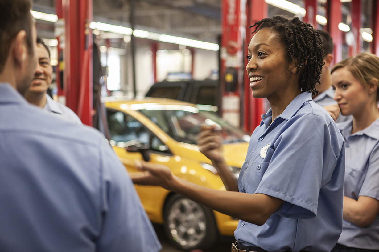 Team of mechanics working on a car discuss a problem in an auto repair shop