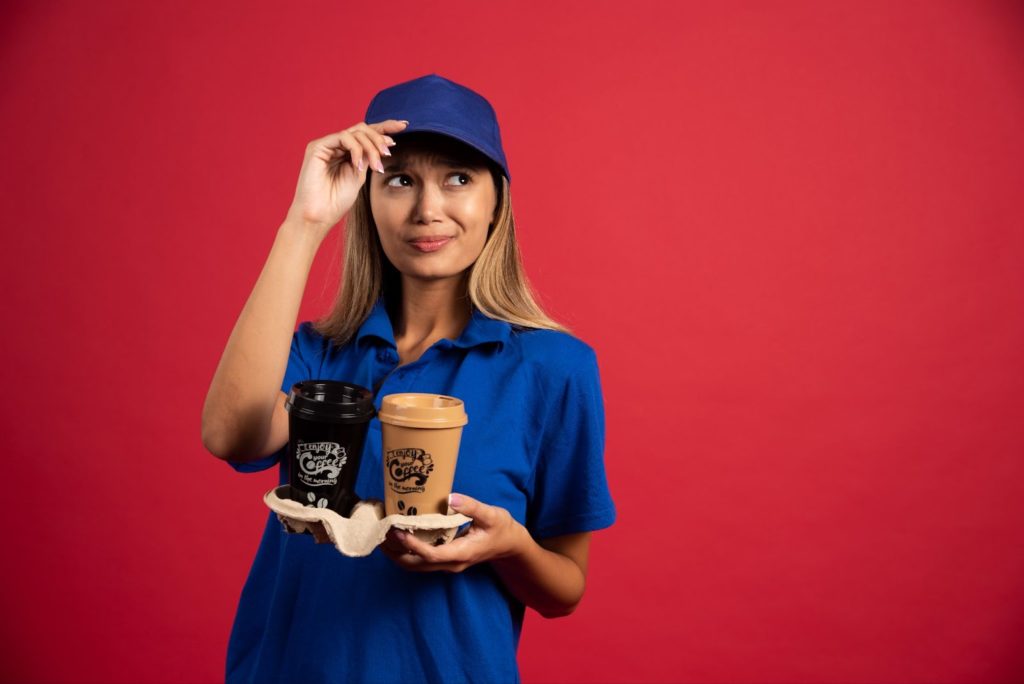 A woman in a blue shirt and cap holding a coffee cup at a coffee shop.