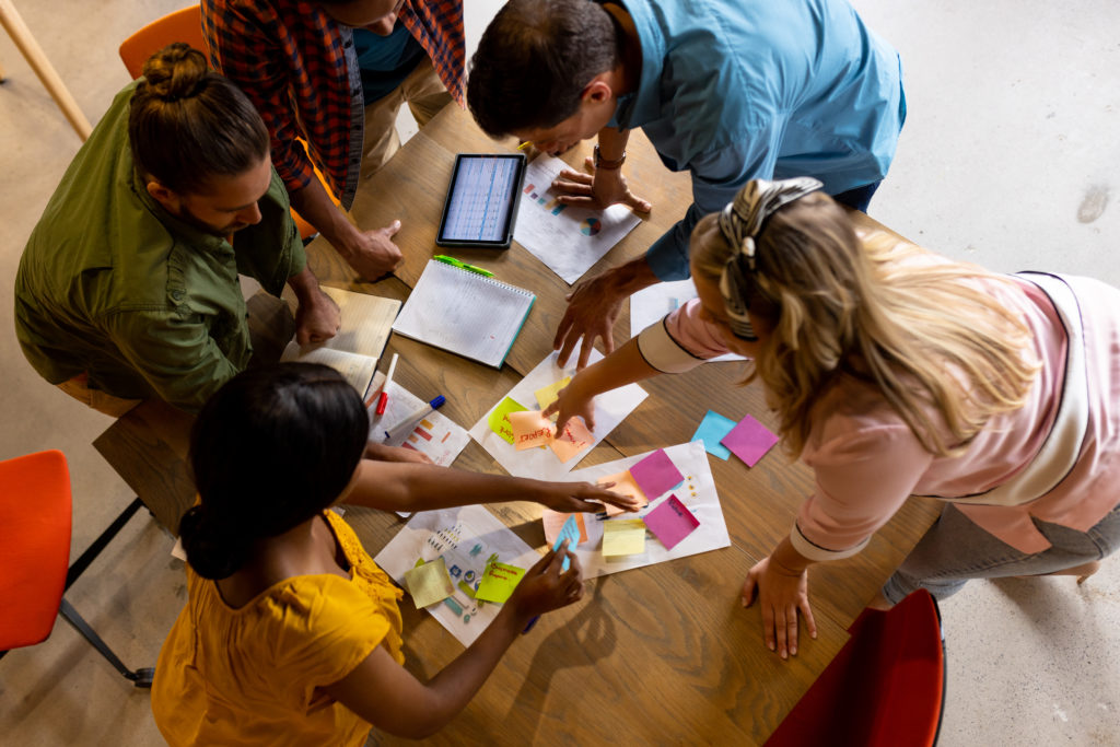 High angle view of diverse creative colleagues in discussion brainstorming using notes and tablet. Casual office, brainstorm, business, teamwork, business and creative work, unaltered.