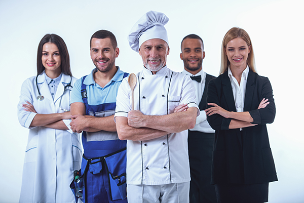 Beautiful people of different professions in uniforms are looking at camera and smiling, isolated on white. Handsome mature cook in the foreground